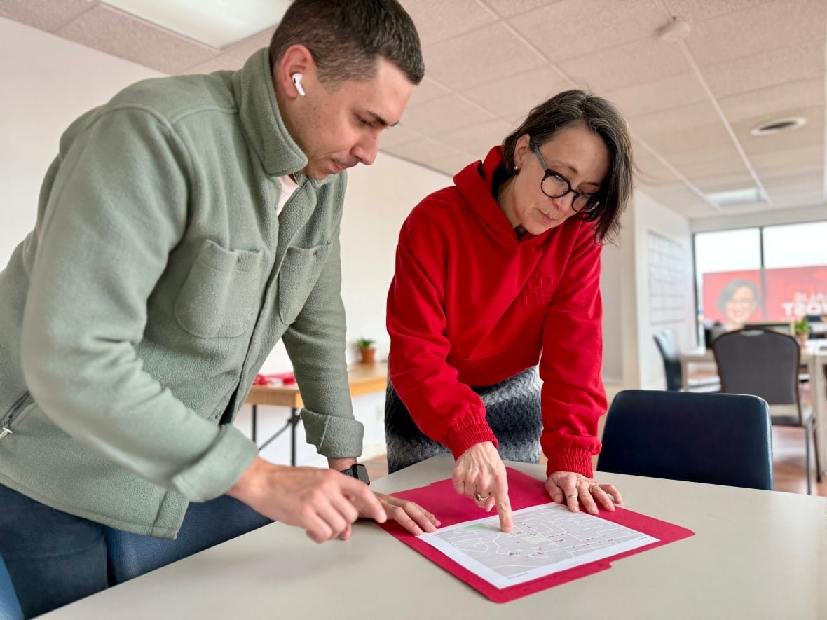 nathalie-provost-campaign-office A woman in a red sweater stands next to a man and points at a document on a table.