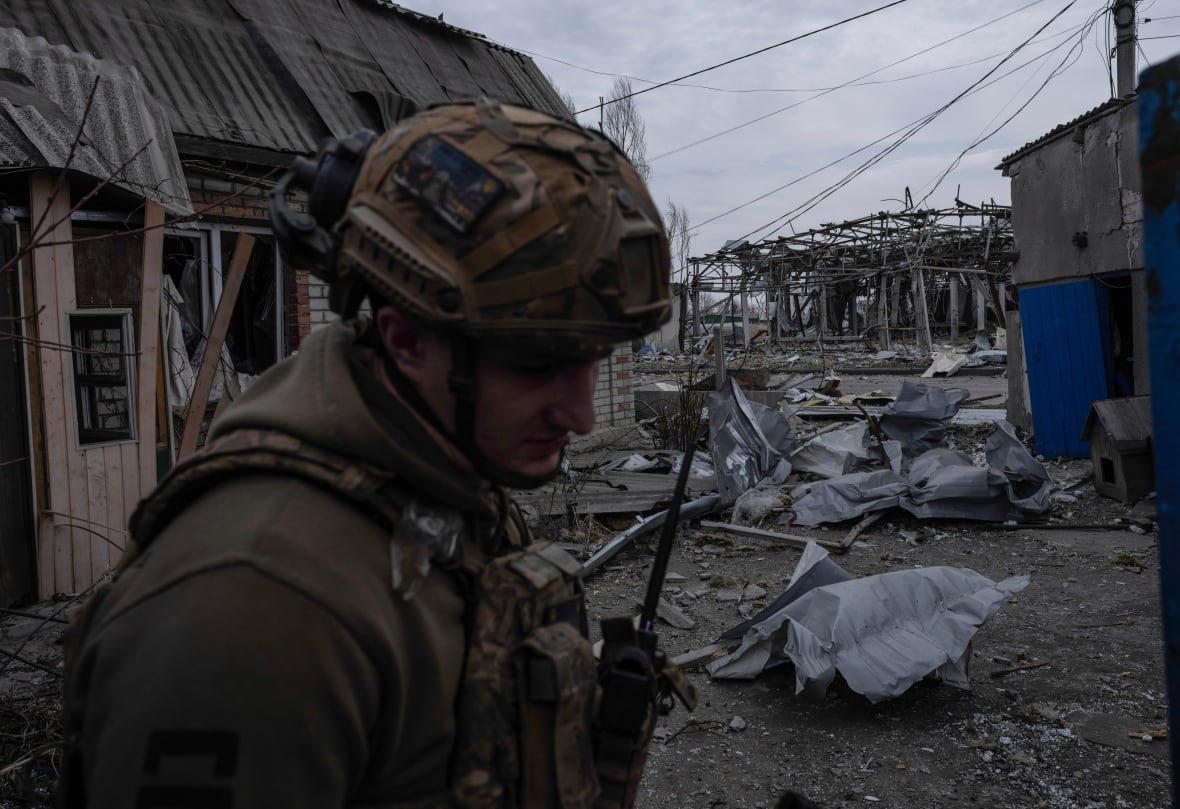 russia-ukraine-war-1 A soldier holding a walkie-talkie stands near destroyed buildings.