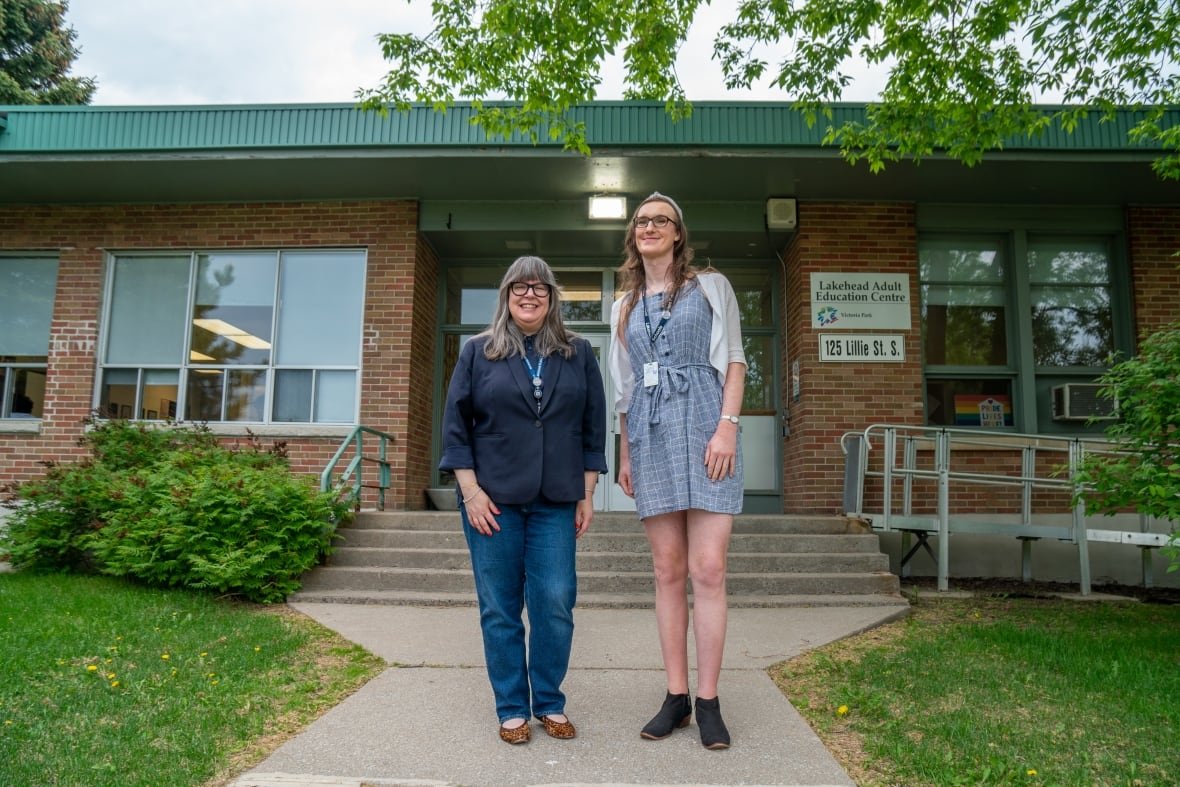 samantha-peotto-and-kara-babcock-1 Two people are seen standing outside a brick building with a dark green roof.