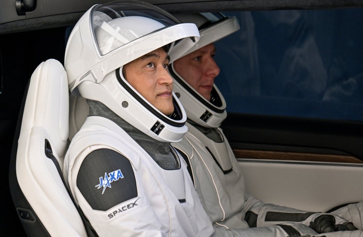 spacex-exploration-crew-10 Two people sit together in a spaceship, both wearing spacesuits.