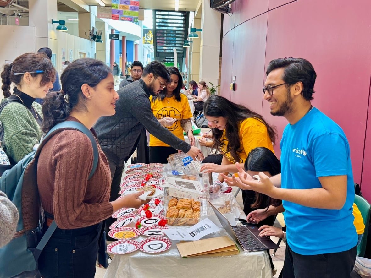 students Students wearing backpacks gather around a table of food.