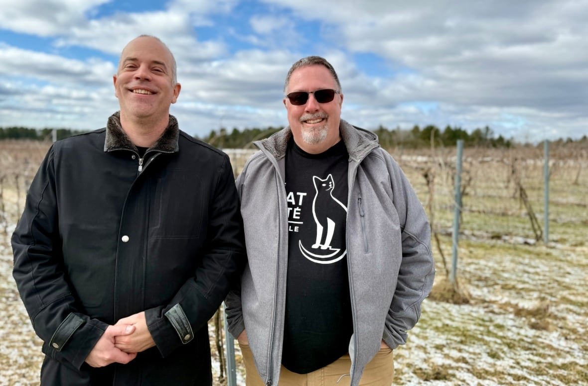 winemakers-in-quebec-riding Two men smile for a photo. The one on the left is wearing a black jacket and the other man is wearing a grey jacket and sunglasses.