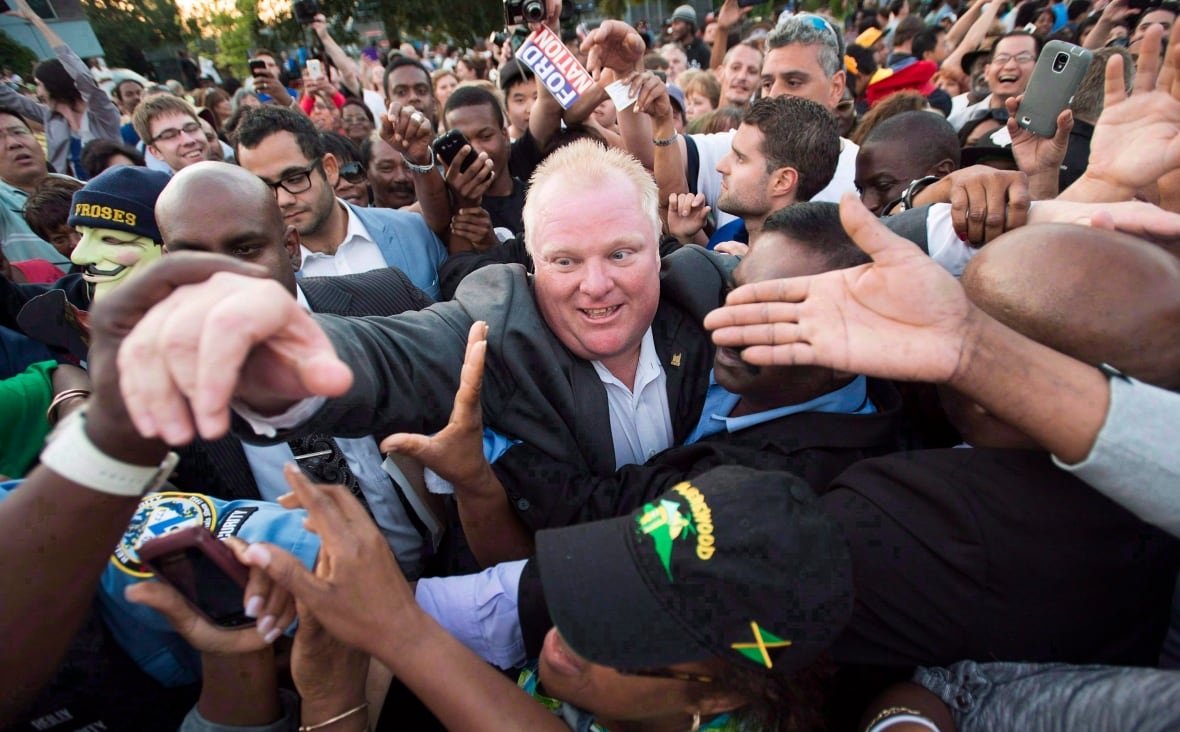 year-cda-deaths-20161228-1 A smiling man reaches forward with an arm raised above the crowd that is surrounding him. He is in a crush of people, some of which are turned towards him with extended hands or phones.
