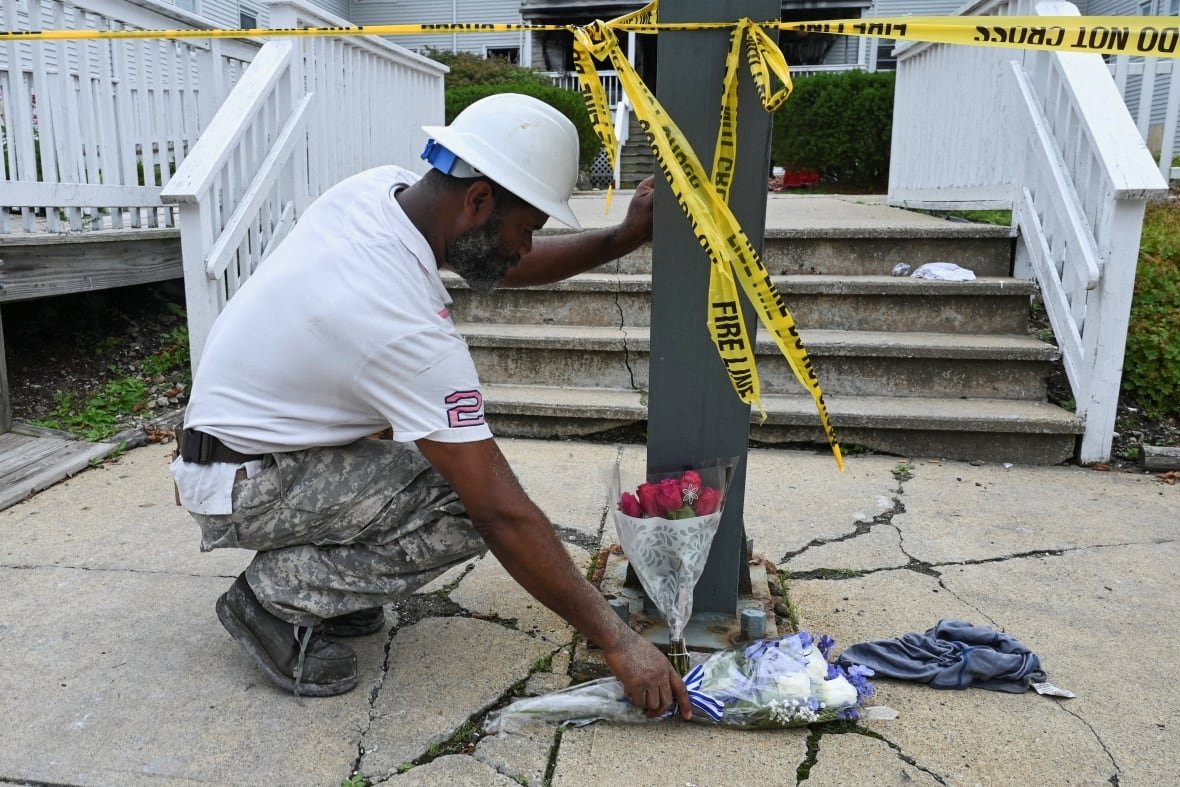 massachusetts-fire-3 A man wearing a white construction hard helmet kneels down and lays blue flowers on a cracked sidewalk.