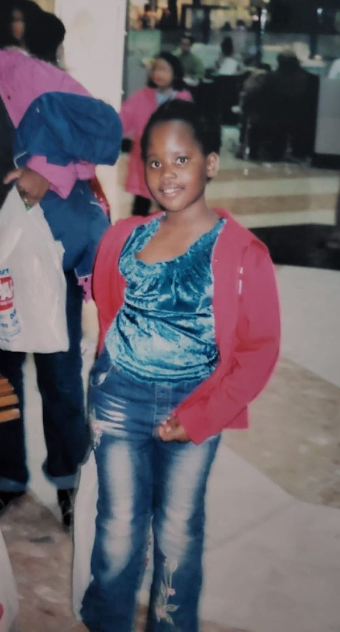 An old photo shows a young Black girl with jeans and a pink cardigan.
