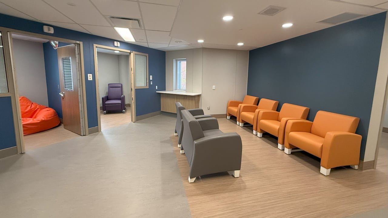 A small medical waiting room with blue walls. Two treatment rooms with open doors are seen, one with a treatment chair and one with a bean bag chair.