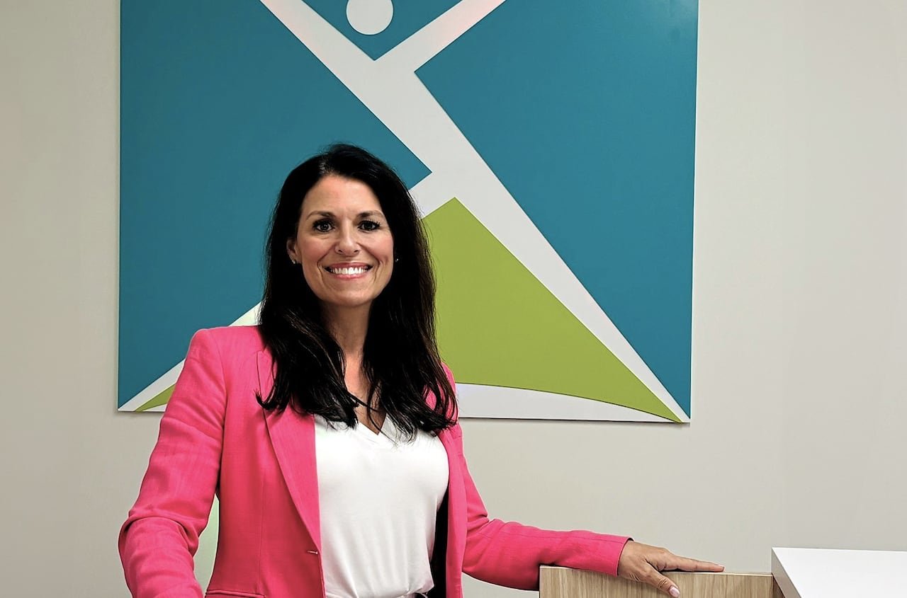 Woman in pink jacket and long brown hair stands in an office.