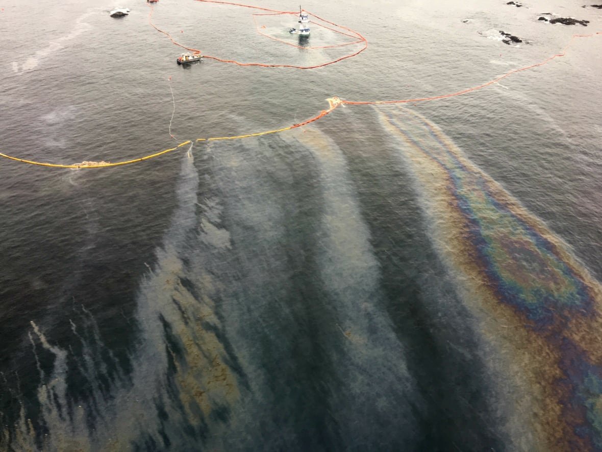 A visible oil slick on blue waters with distant boats.