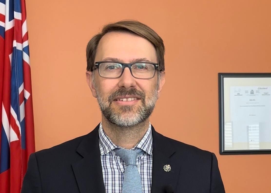 A man in a suit smiles for the camera against a wall.