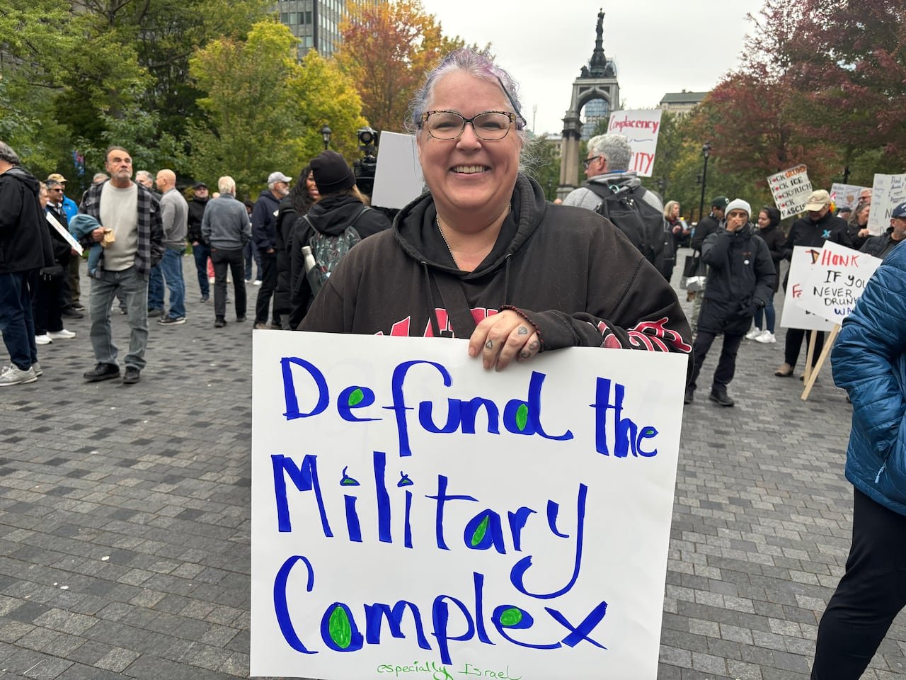 A woman holds a sign that reads: 'Defund the military complex.'