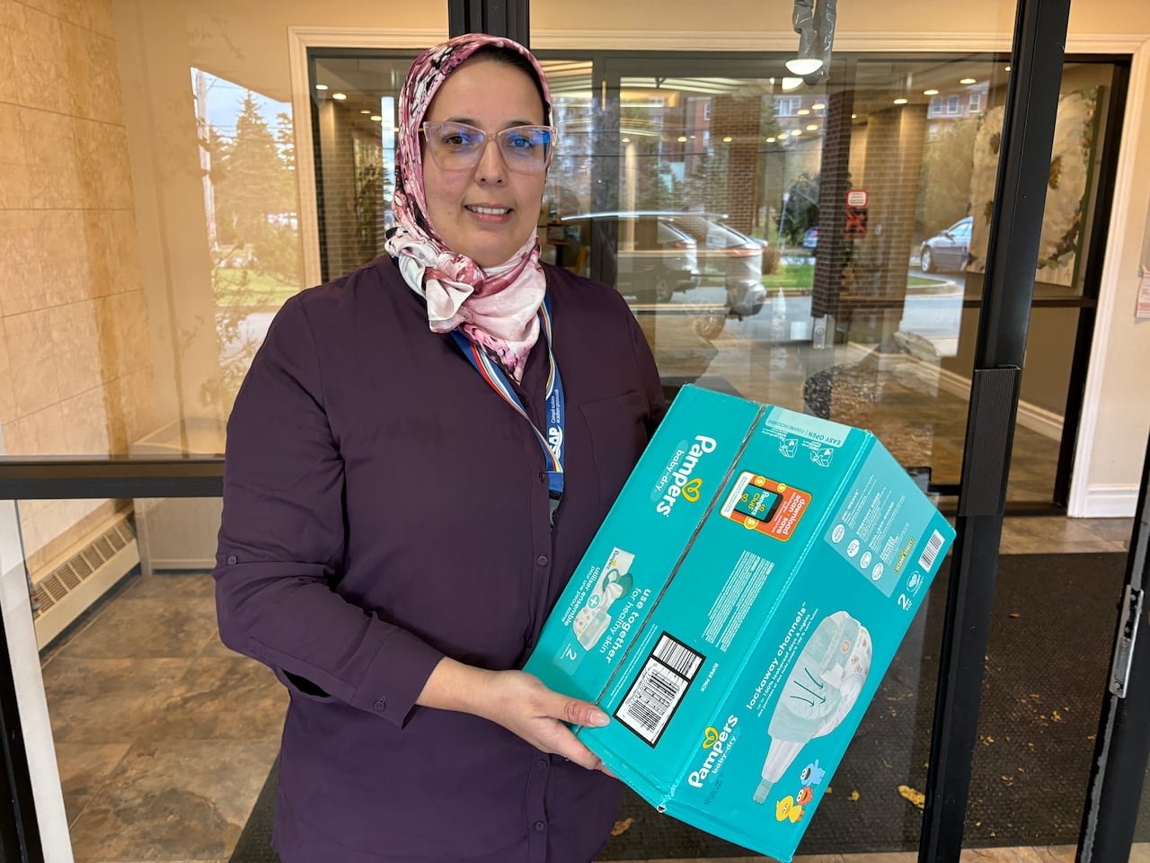 A woman holds a large box of diapers.