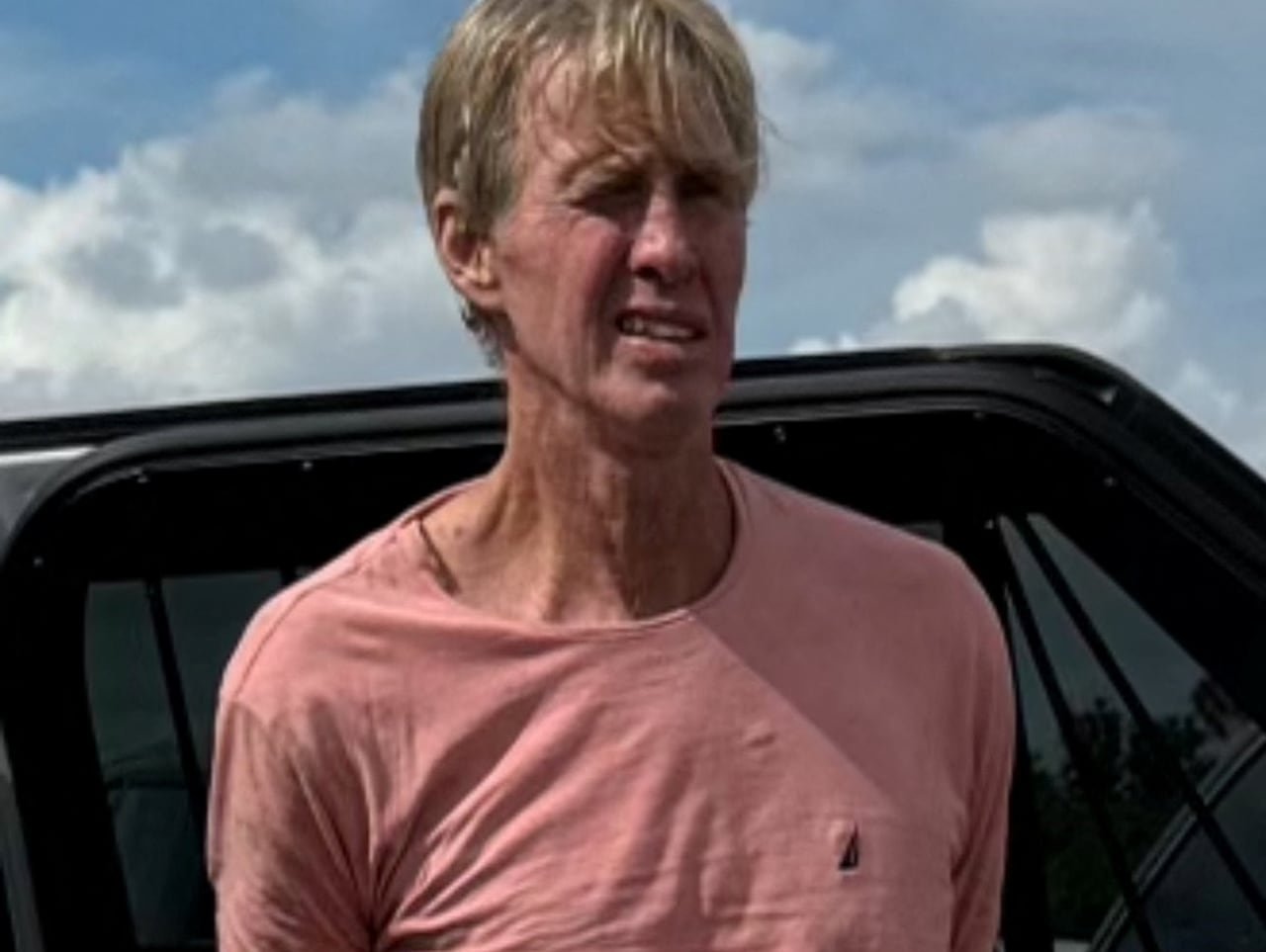 Man in pink top with hands behind his back