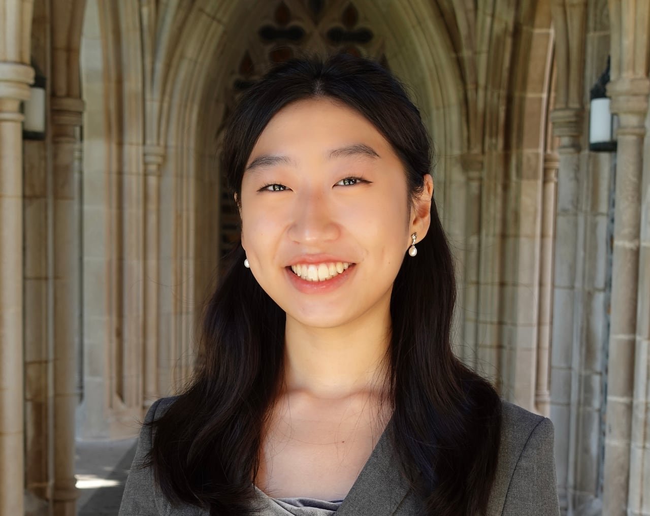 default-2438 A smiling student in a gray blazer standing in a stone alcove.
