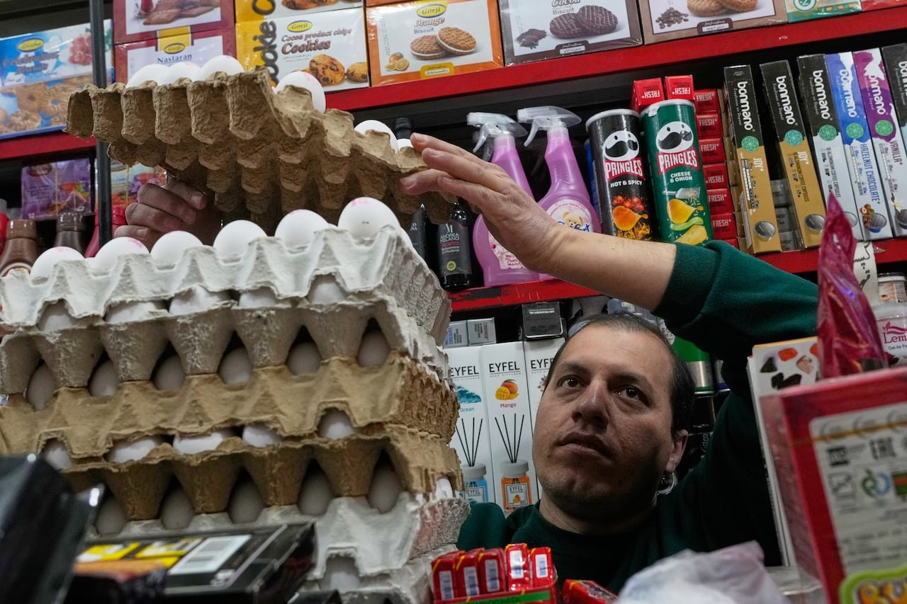 A man stands in front of a display of grocery items and arranges crates of eggs