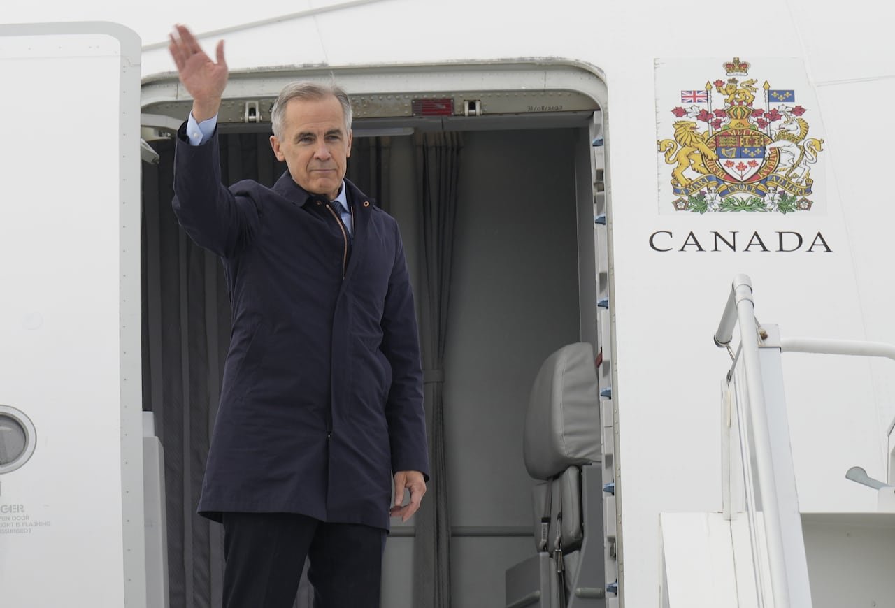 Carney waves from outside the door of a Canadian government airplane.