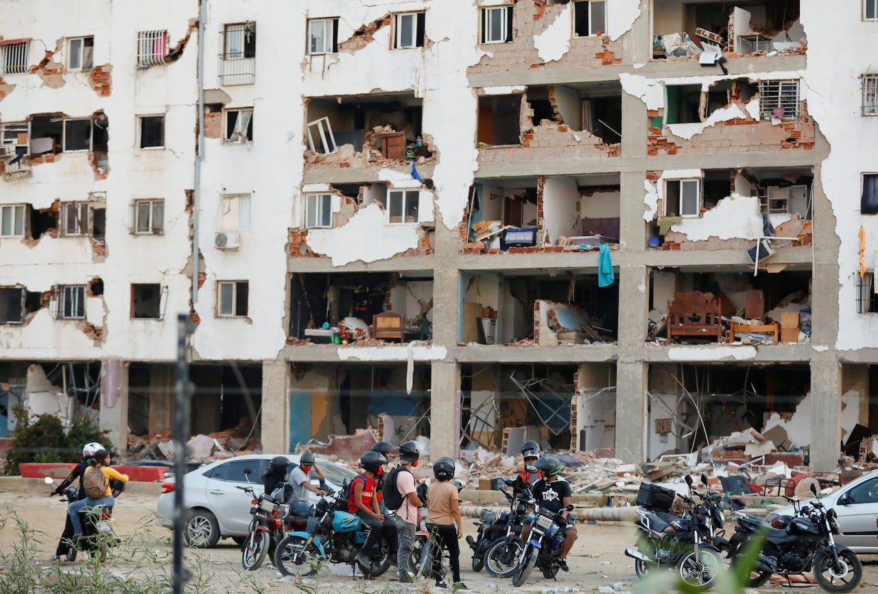 default-147 People in motorcycle helmets look at the remains of a building.
