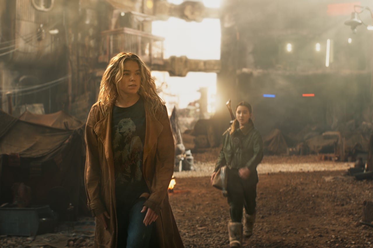 A woman and girl walk down a dirty, alien-looking street.