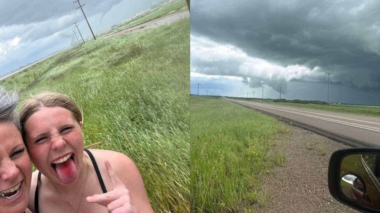 Two people in a field with a small funnel cloud in the background.