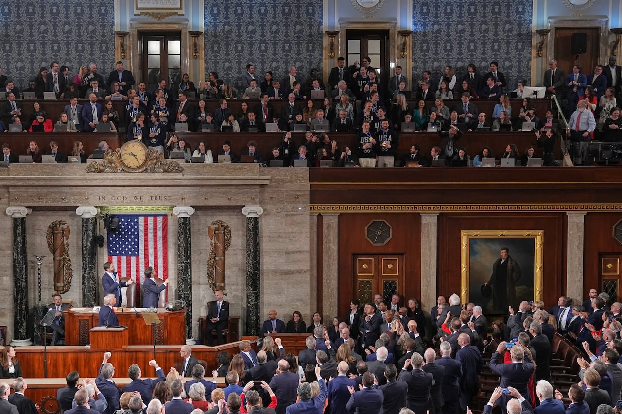 default-461 Members of the House of Representatives stand and applaud, while looking up at a group of men standing in the gallery wearing USA Olympic pullovers.